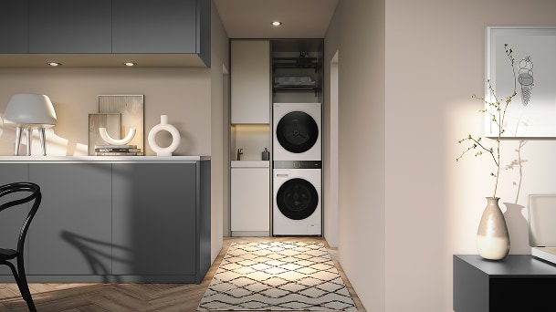 „LG WashTower“ skalbyklė šiltame minimalistiniame prieškambario skalbyklos kampelyje su pilkomis spintelėmis, raštuotu kilimėliu ir švelniu apšvietimu.